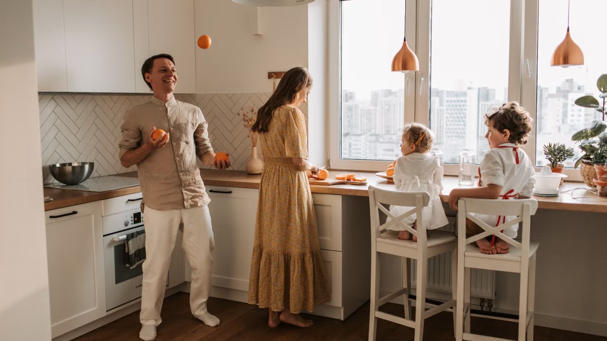 Family enjoying a playful morning in a sunlit modern kitchen with city view.